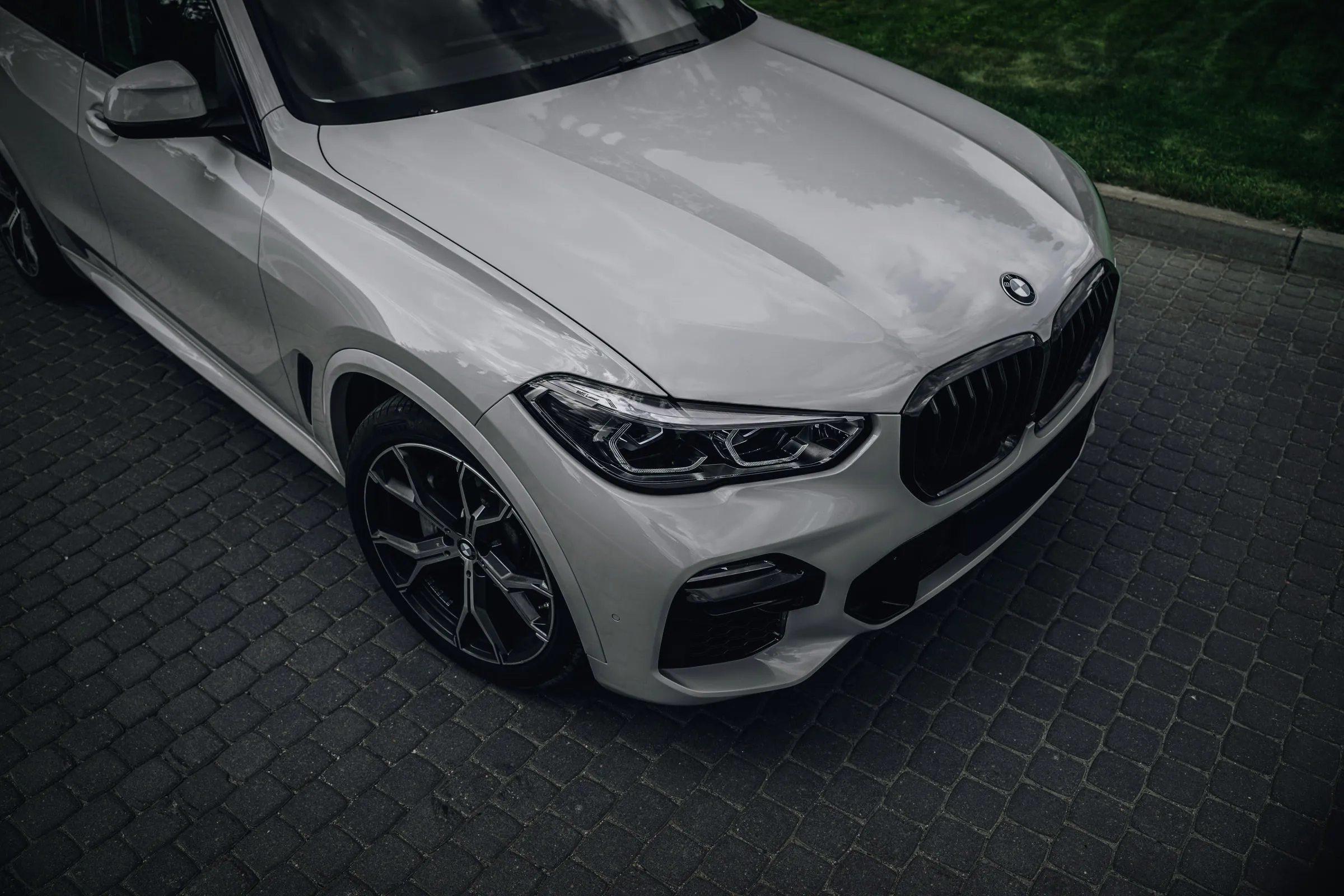 Предниот агол на белиот BMW X5 одозгора: хаубата, фарот и решетката.