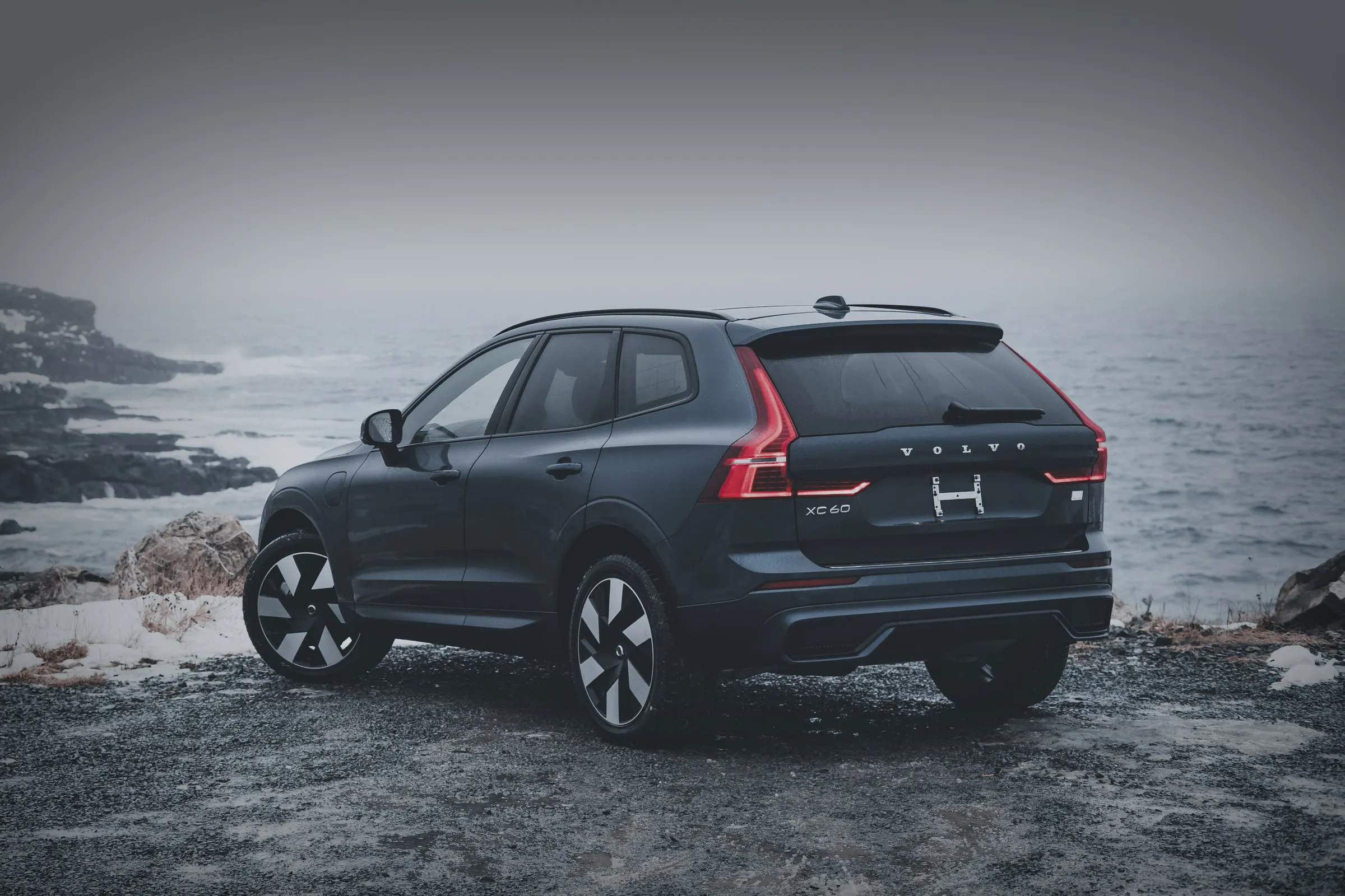 Темно сино-сив Volvo XC60 гледан одзади и од страна, на брег над зимско море.